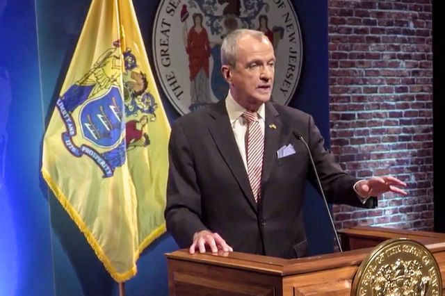 Governor Phil Murphy in a screenshot of his state of the state; he is wearing a suit and standing at a lectern in from of the NJ flag and state seal